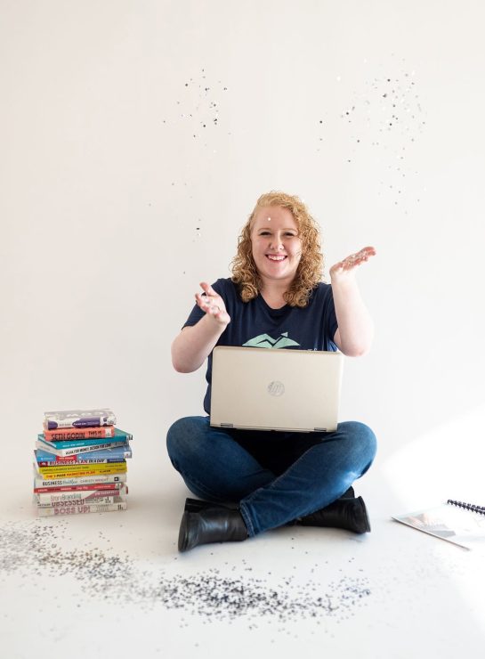 Hailey Fackrell throwing confetti in the air with laptop and stack of books