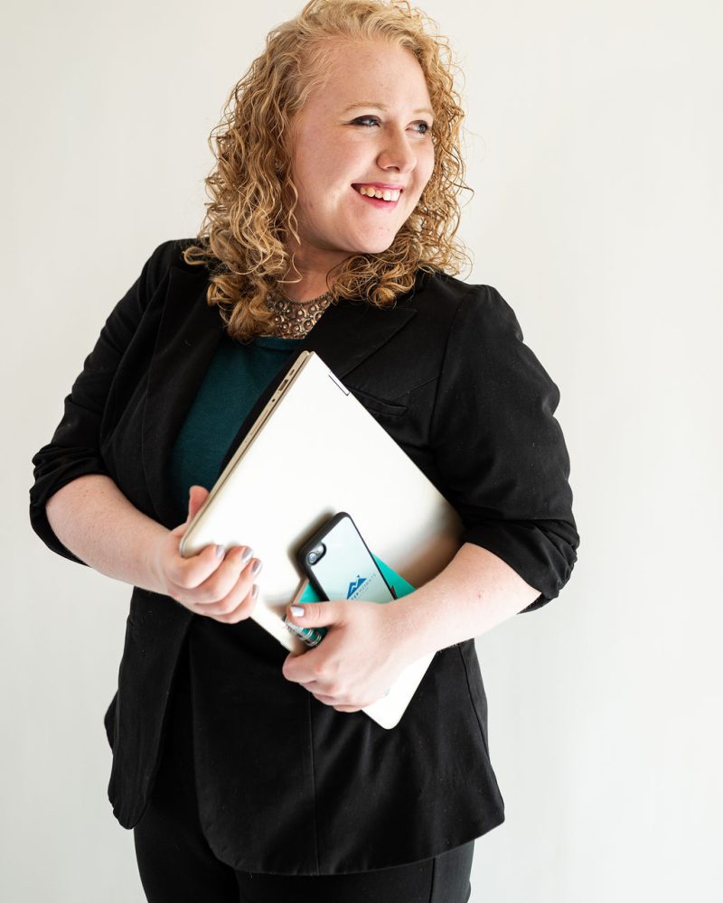 Hailey Fackrell looking off into the distance, holding phone, laptop and notebook