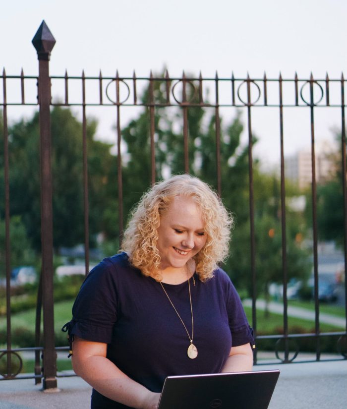 Hailey Fackrell working on computer in front of fence outside